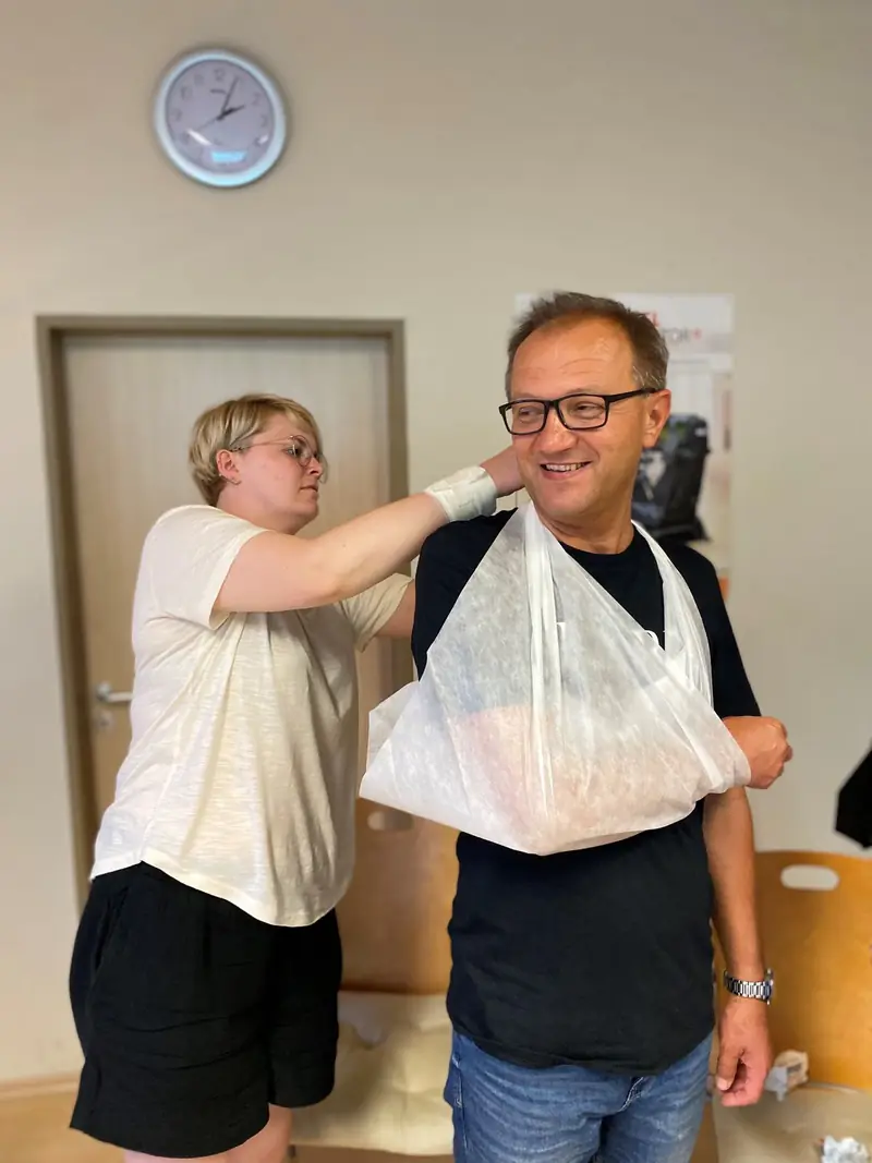 Erste-Hilfe-Ausbilderin legt einem Teilnehmer eine Armschlinge an