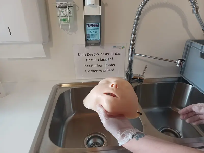 Gesichtsteil einer Übungspuppe wird im Lager am Waschbecken gereinigt