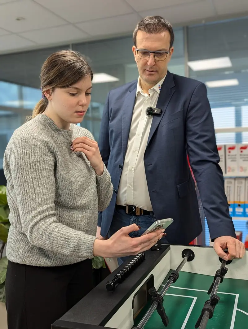 Zwei Kollegen schauen am Kickertisch im Büro gemeinsam aufs Handy