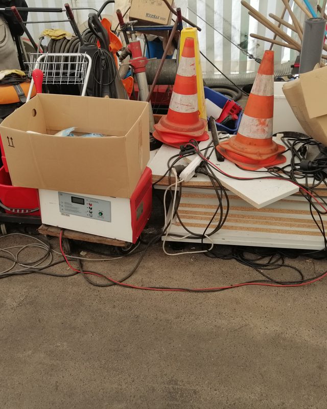 Laufendes Ladegerät zwischen Kartons, Kabeln und abgestelltem Material
