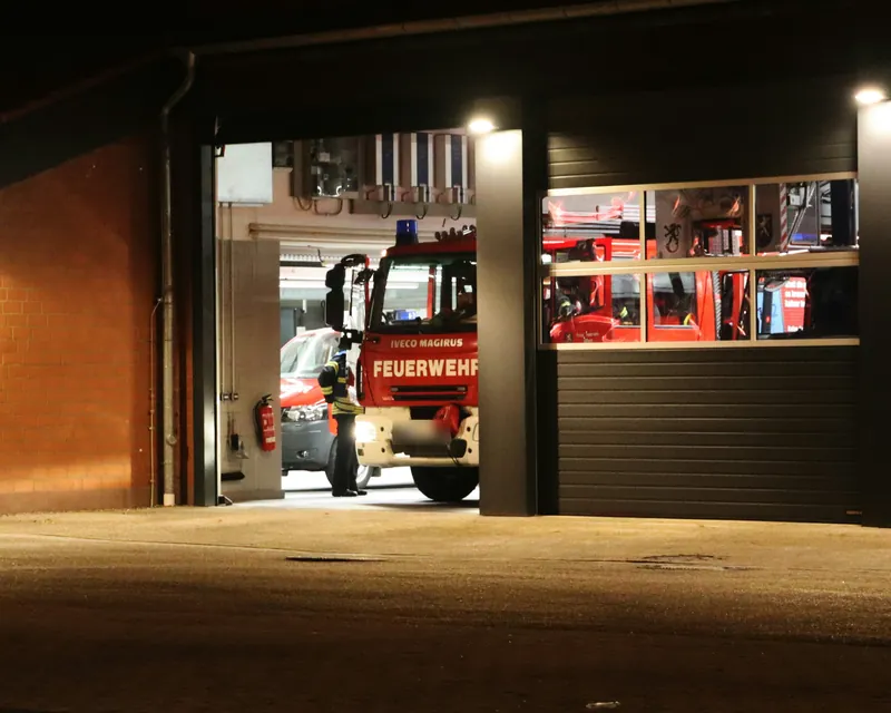 Feuerwehrhaus bei Nacht mit offenem Tor und Löschfahrzeug in der Fahrzeughalle